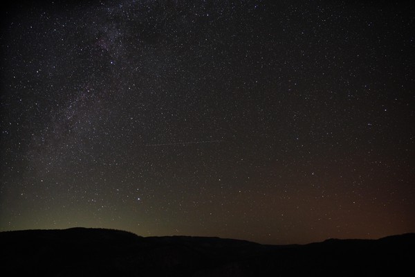Starry night sky with ambient red and green light from the mountains below